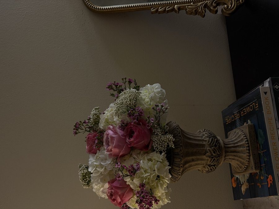 Pink rose and white hydrangea arrangement in an ornate urn beside a gold mirror in moody light
