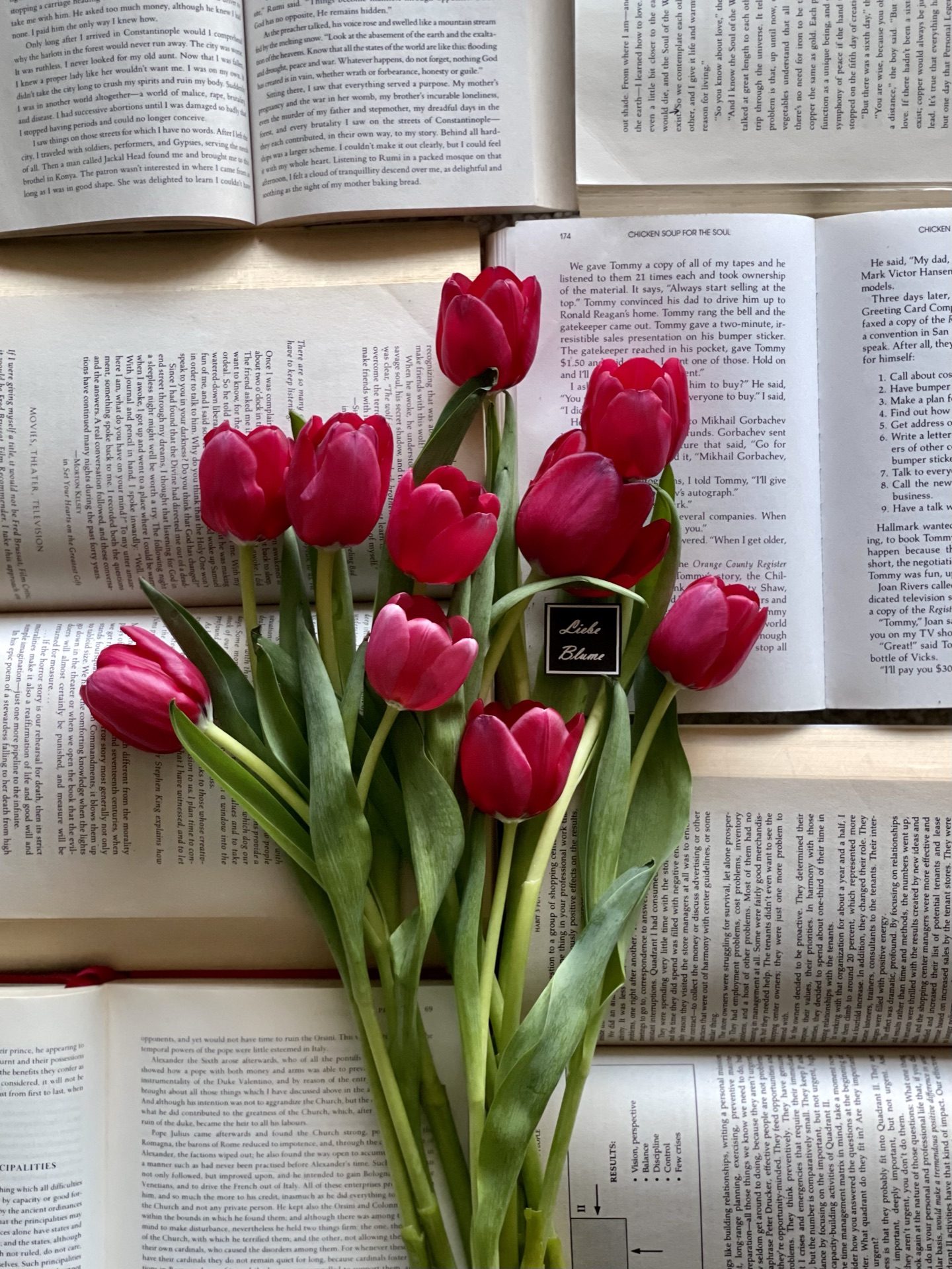 Magenta tulips with a black Liebe Blüme tag laid across open book pages